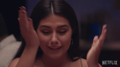A Woman Is Smiling With Her Hands On Her Face In Front Of A Netflix Sign GIF