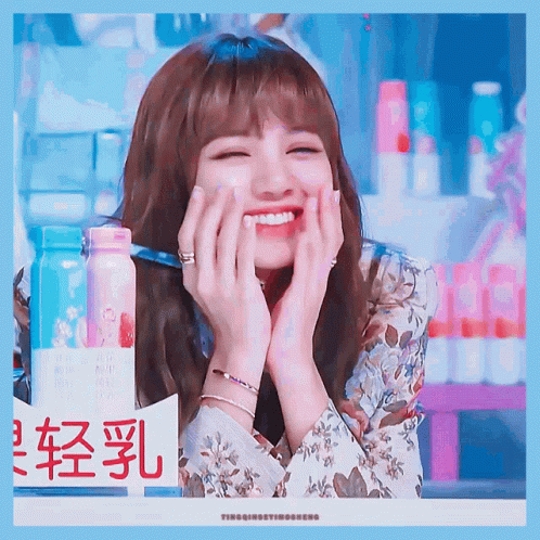 A Woman Is Smiling With Her Hands On Her Face In Front Of A Sign With Chinese Characters GIF