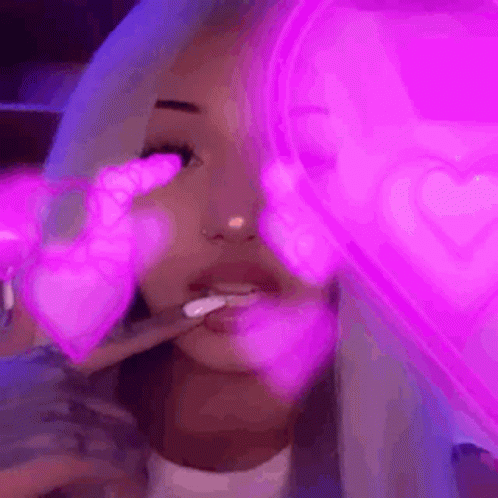 A Woman Is Smoking A Cigarette In Front Of A Neon Heart . GIF