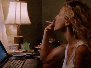 A Woman Is Smoking A Cigarette While Looking At A Laptop GIF