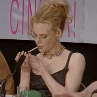 A Woman Is Smoking A Cigarette While Sitting At A Table In Front Of A Sign That Says Cinema . GIF