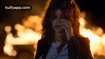 A Woman Is Smoking A Cigarette While Standing In Front Of A Fire At Night . GIF