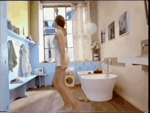 A Woman Is Standing In A Bathroom With A Bathtub GIF