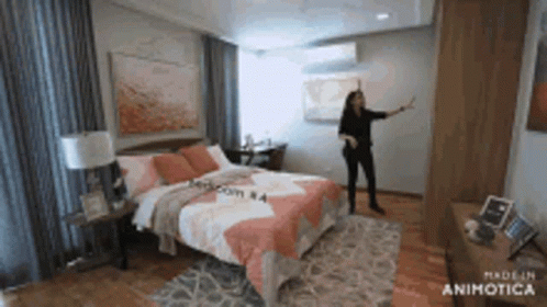 A Woman Is Standing In A Bedroom With A Large Bed . GIF