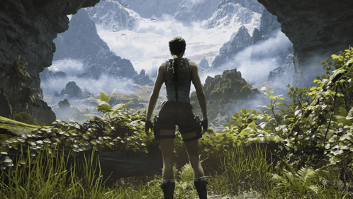 A Woman Is Standing In A Cave Looking Out At A Mountain Range GIF