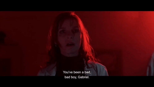A Woman Is Standing In A Dark Room And Talking To A Boy . GIF