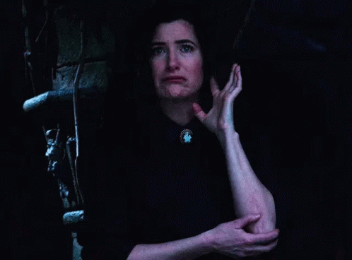 A Woman Is Standing In A Dark Room Holding Her Elbow . GIF