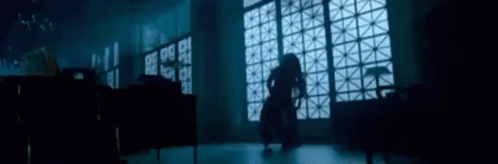 A Woman Is Standing In A Dark Room In Front Of A Large Window . GIF