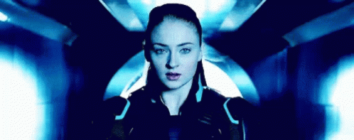 A Woman Is Standing In A Dark Room With A Blue Light Behind Her And Looking At The Camera . GIF