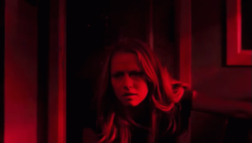 a woman is standing in a dark room with a red light behind her .