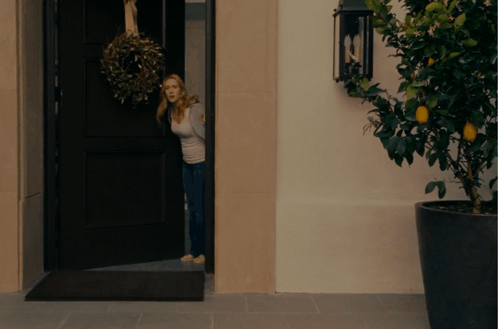 A Woman Is Standing In A Doorway With A Wreath Hanging From It GIF