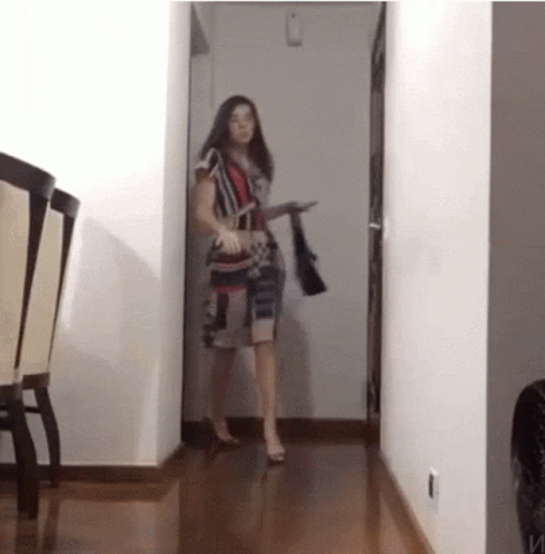 A Woman Is Standing In A Hallway Holding A Purse GIF