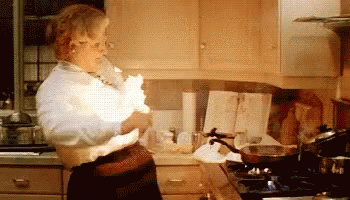 A Woman Is Standing In A Kitchen Holding A Piece Of Paper That Is Exploding . GIF