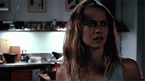 A Woman Is Standing In A Kitchen Wearing A White Tank Top GIF