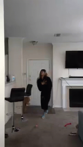 A Woman Is Standing In A Living Room In Front Of A Fireplace And Television . GIF
