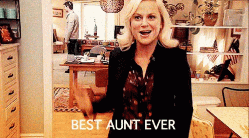 A Woman Is Standing In A Living Room With The Words `` Best Aunt Ever '' On Her Shirt . GIF