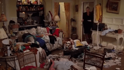 A Woman Is Standing In A Messy Living Room Filled With Lots Of Clothes And Papers . GIF