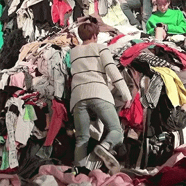 A Woman Is Standing In A Pile Of Clothing GIF
