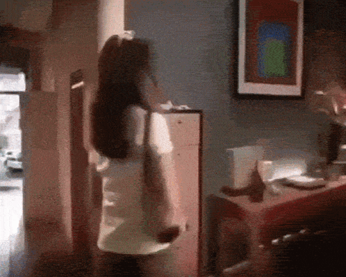 A Woman Is Standing In A Room With A Picture On The Wall Above Her GIF