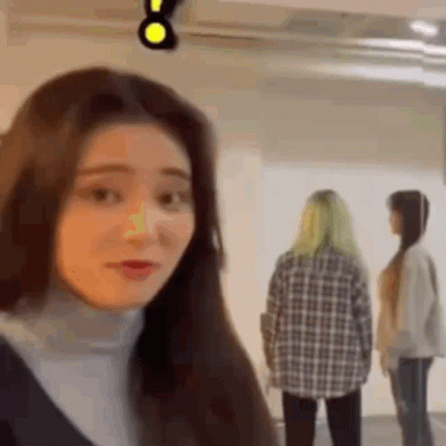 A Woman Is Standing In A Room With Two Other Women And Looking At The Camera . GIF