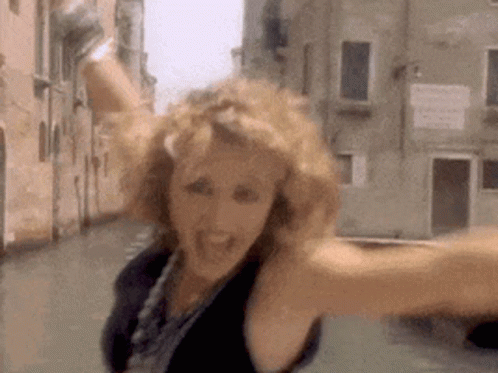 A Woman Is Standing In A Street With Her Arms Outstretched And A Building In The Background . GIF