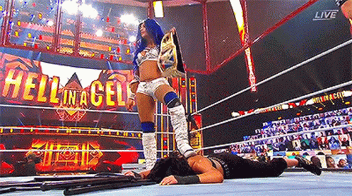 a woman is standing in a wrestling ring holding a championship belt while another woman is laying on the ground .