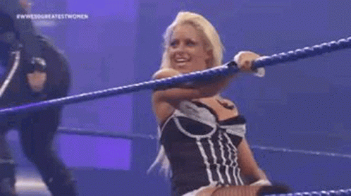 A Woman Is Standing In A Wrestling Ring Holding A Rope And Smiling . GIF