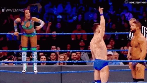 A Woman Is Standing In A Wrestling Ring With A Referee And A Man Standing Behind Her . GIF