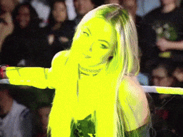 A Woman Is Standing In A Wrestling Ring With Her Arms Outstretched In Front Of A Crowd GIF