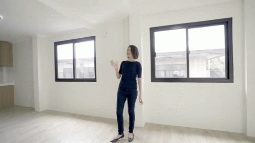 A Woman Is Standing In An Empty Room With A Lot Of Windows GIF