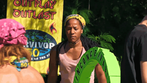 A Woman Is Standing In Front Of A Banner That Says Outplay Outlast GIF