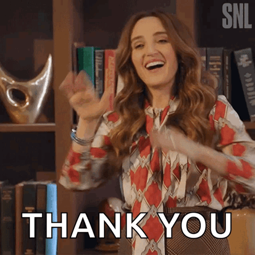 A Woman Is Standing In Front Of A Bookshelf And Giving A Thank You Sign GIF