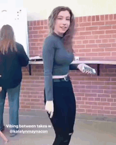 A Woman Is Standing In Front Of A Brick Wall And Holding A Bottle Of Water . GIF