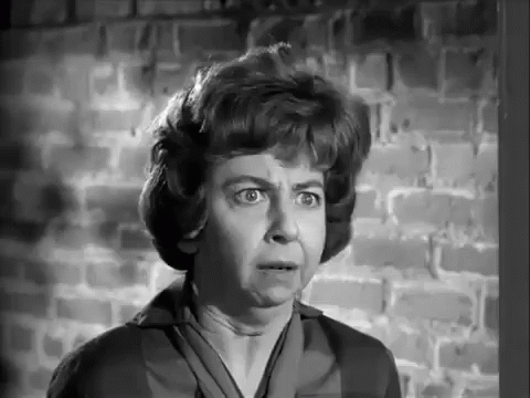 A Woman Is Standing In Front Of A Brick Wall Making A Funny Face . GIF
