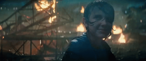 A Woman Is Standing In Front Of A Burning Building In A Dark Room . GIF