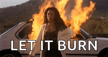 A Woman Is Standing In Front Of A Car On Fire . GIF