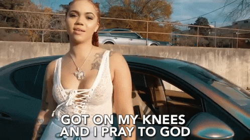 A Woman Is Standing In Front Of A Car With The Words `` Got On My Knees And I Pray To God '' GIF