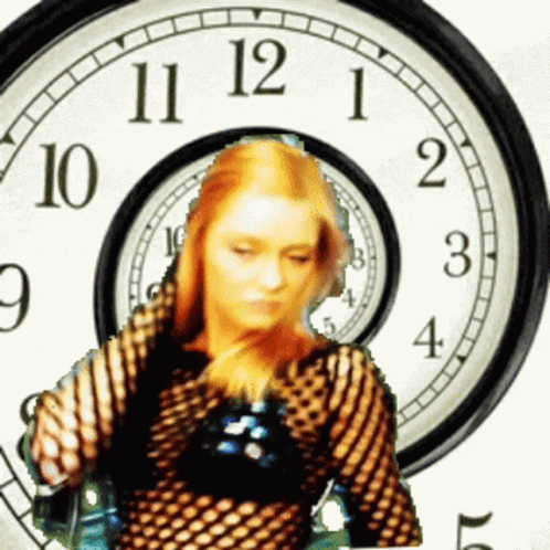 A Woman Is Standing In Front Of A Clock With The Hands On The Numbers 11 12 And 1 GIF