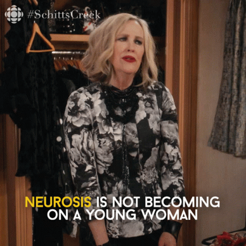 A Woman Is Standing In Front Of A Closet With The Words " Neurosis Is Not Becoming On A Young Woman " Written Below Her GIF