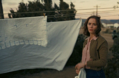 A Woman Is Standing In Front Of A Clothesline With A White Cloth Hanging On It GIF
