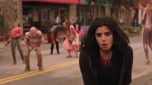 A Woman Is Standing In Front Of A Crowd Of Zombies . GIF