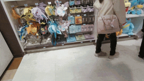 A Woman Is Standing In Front Of A Display Of Stuffed Animals Including One That Says Eevee GIF