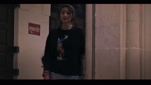 A Woman Is Standing In Front Of A Door In A Dark Room . GIF