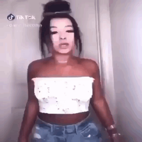 A Woman Is Standing In Front Of A Door Wearing A White Top And Blue Jeans . GIF