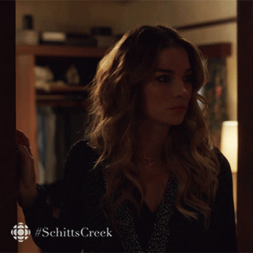 A Woman Is Standing In Front Of A Door With #Schitts Creek Written On The Bottom GIF