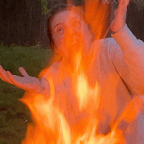 A Woman Is Standing In Front Of A Fire With Flames Coming Out Of Her Face GIF