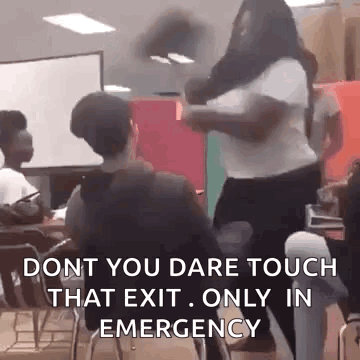 A Woman Is Standing In Front Of A Group Of People In A Classroom While A Man Sits In A Chair . GIF