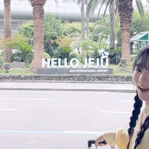 A Woman Is Standing In Front Of A Hello Jeju Sign GIF