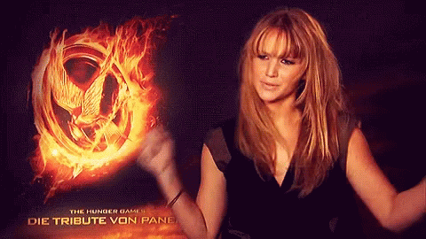 A Woman Is Standing In Front Of A Hunger Games Poster GIF