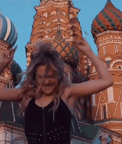 A Woman Is Standing In Front Of A Large Building With Her Hair In The Air . GIF